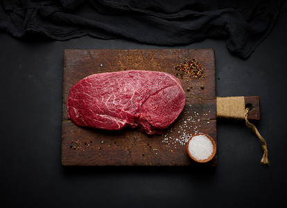 生牛里脊肉放在切菜板上，香料放在黑桌上，俯视