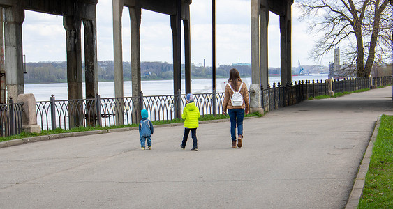 小孩散步摄影照片_在一个晴朗的春日，一位母亲和两个小孩沿着堤岸散步