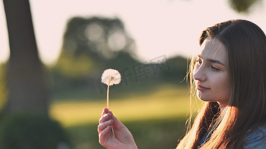一个年轻的女孩轻轻地看着蒲公英花。