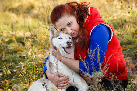 狗饲养员在秋天的森林里拥抱着她的哈士奇狗