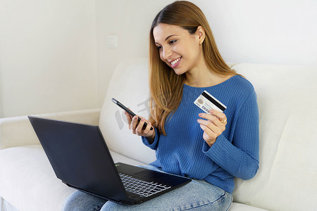 巴西妇女持有信用卡和智能手机，使用笔记本电脑在家网上购物。 