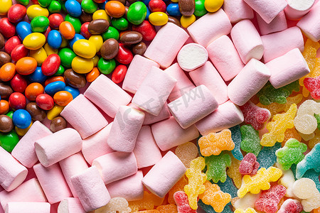 小熊软糖果香摄影照片_软糖、彩色巧克力球和棉花糖的特写，它们排列成三条对角线，占据了整个水平图像