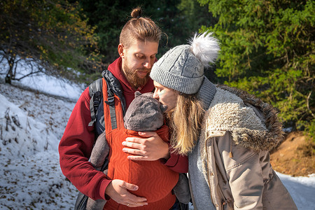 在冬季户外探险中，带着婴儿的年轻家庭穿着符合人体工学的婴儿背带