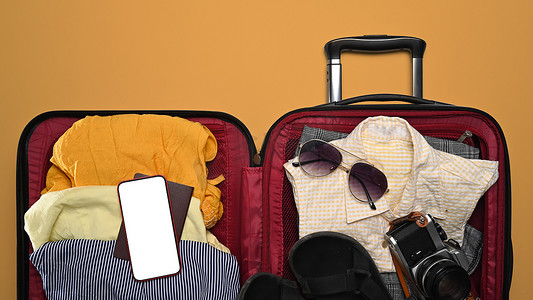 暑假在黄色背景下打开手提箱、智能手机、太阳镜、相机和护照。