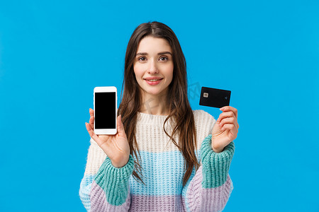银行账户摄影照片_腰部向上肖像自信的年轻女性微笑着，展示银行系统如何运作，将银行账户与智能手机应用程序连接，持有信用卡和手机，展示一些东西