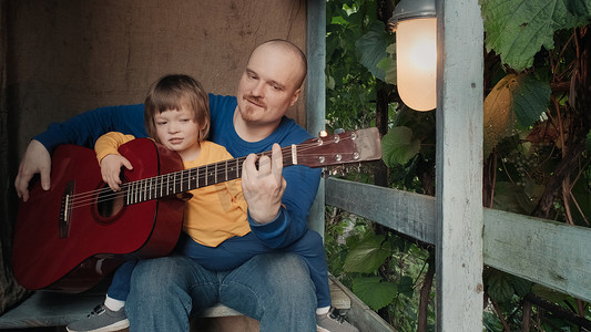 弹吉他的小孩摄影照片_爸爸为他的小孩弹一把原声吉他。