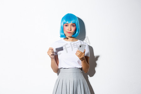 优柔寡断的亚洲女孩形象，打扮成动漫人物，戴着蓝色假发，拿着信用卡和手机，思考或做出决定，站在白色背景上