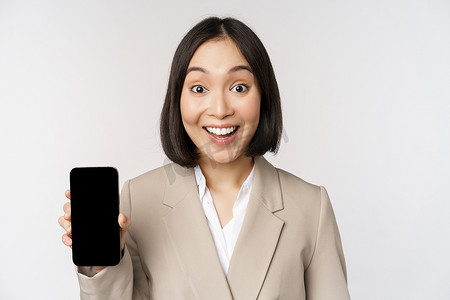亚洲企业女性展示应用程序界面、手机屏幕、做出惊讶的表情、哇，站在白色背景上