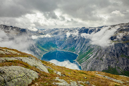 霍达兰摄影照片_蓝色的湖泊，周围环绕着陡峭的悬崖，隐藏在云层中，奥达，霍尔