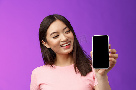 高兴的快乐漂亮的亚洲年轻女性微笑着满意地拿着智能手机，显示手机屏幕看起来手机显示很高兴，介绍应用程序，展示应用程序，紫色背景