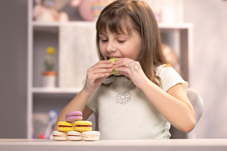 一个小女孩快乐的笑脸在家庭背景下玩甜点马卡龙。