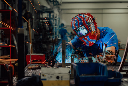 在工厂内工作的专业重工业焊工，戴着头盔并开始焊接。