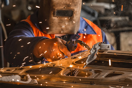 戴着防护面罩的焊工工业工人用火花进行焊接工作，并在工厂车间修理车门