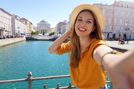 年轻的女游客站在桥上自拍，欣赏意大利的里雅斯特市的美景