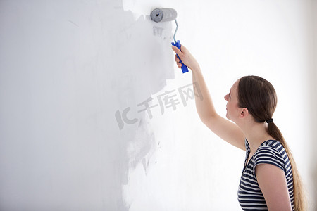 家里墙壁摄影照片_年轻女子在家里粉刷墙壁