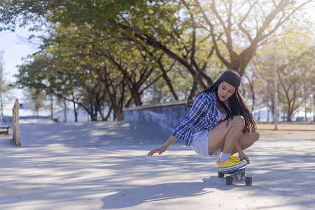 年轻的亚洲女性早上在户外的公园滑板坡道上玩冲浪滑板。