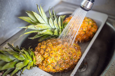 下水槽摄影照片_两个成熟多汁的菠萝在水槽的水龙头下清洗。