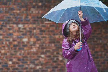 孩子伞摄影照片_下雨了，倾盆大雨......一个小女孩站在外面伞下的镜头。