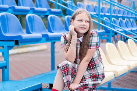 蓝色校服摄影照片_学校体育场蓝黄相间的看台上穿着校服的漂亮女孩。
