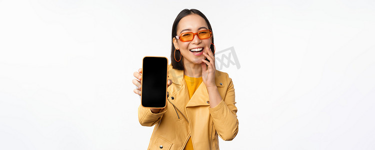界面购物摄影照片_热情的亚洲女模特，在手机屏幕上展示智能手机应用程序界面、在线商店或网站，站在白色背景上