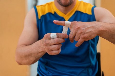 一名残疾篮球运动员穿上紧身胸衣，在手臂和手指上缠上绷带，准备在竞技场上进行比赛