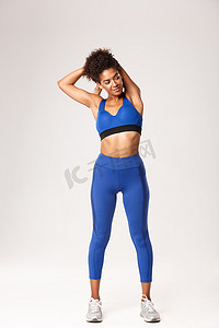 全长美丽微笑的非洲裔美国女运动员，穿着蓝色运动服，锻炼前热身，展示伸展运动，白色背景