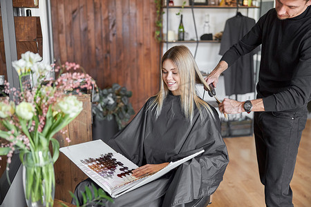 金发女客户正在选择书中的颜色，而美发师正在剪头发