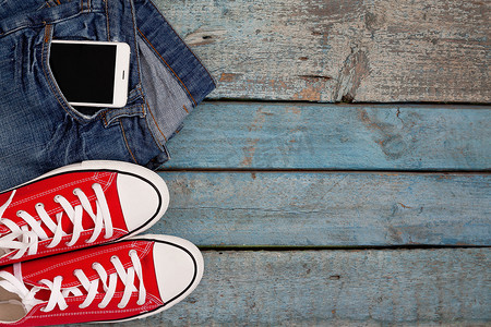 蓝色复古牛仔裤口袋里的红色复古运动鞋和智能手机