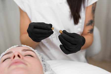 一位戴着黑色无菌手套的美容医生在年轻化手术前打开装有透明质酸的安瓿的特写。