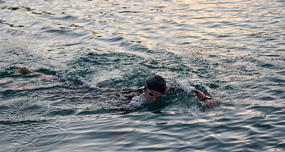 日出时穿着潜水服在湖上游泳的铁人三项运动员