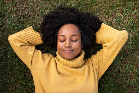 草地俯视图摄影照片_年轻的非洲裔美国妇女闭着眼睛躺在草地上休息。