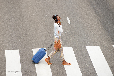 非洲裔美国妇女背着旅行包和手机过马路的侧面肖像