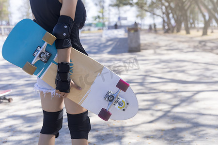 特写年轻女性穿着保护和手持滑板，在公共滑板坡道公园背景上滑冰。