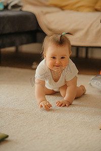 一个 7 个月大的女孩在家里爬着沙发，微笑着。