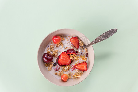一碗牛奶什锦早餐和酸奶配新鲜樱桃、草莓。减肥早餐-一碗绿色背景的燕麦片、浆果和新鲜牛奶。