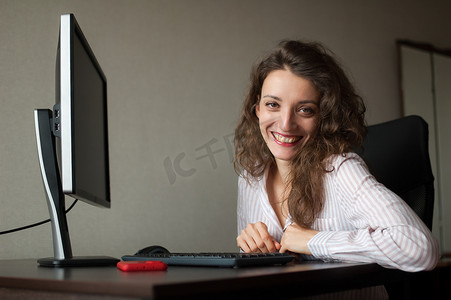 身穿白衬衫和卷发的年轻女办公室经理坐在桌边，用键盘打字，日常工作，自由职业