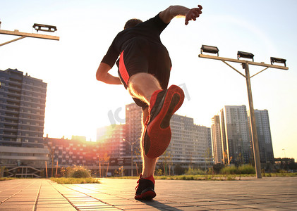 跑步运动的人摄影照片_跑步者的脚在路上奔跑，特写在鞋子上，在日落或日出时在户外