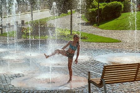 在阳光明媚温暖的日子里，女孩在外面的喷泉里玩耍。