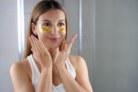 美丽的女孩在浴室里用金色抗衰老眼膜照镜子。