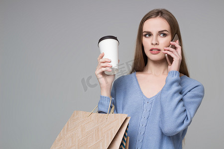 穿蓝色衣服、拎着袋子喝咖啡的女孩用智能手机说话
