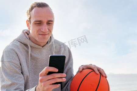 蓝帽技术摄影照片_拿着篮球微笑的男人用手机