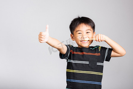 5-6 岁的可爱小男孩微笑着刷牙，竖起大拇指表示好兆头