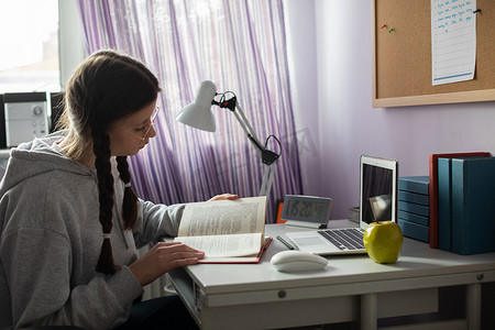 一个梳着辫子戴眼镜的学生在家看书。