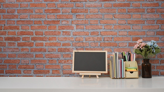 空白的小黑板和白桌上的用品靠在砖墙上，带有用于隔离短信或产品的复制空间。