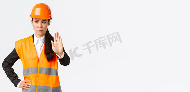 表情严肃、失望的亚洲女建筑师、工作区的施工经理戴着安全帽，表现出停止手势、禁止行动、禁止侵入、白色背景
