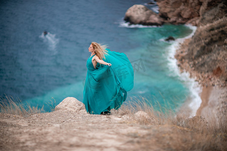 飞舞的丝绸摄影照片_身着翡翠裙的女子，长着丝绸长翅膀的时装模特，飘逸的长裙，飞舞的布料在堤岸上。