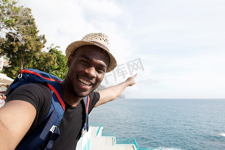 背包的行人摄影照片_微笑的非洲裔美国旅行人在海边自拍并指指点点