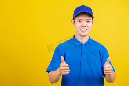 送货快乐的人站着，他微笑着穿着蓝色 T 恤和帽子制服展示拇指手势