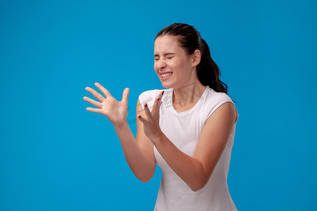 一位身穿白色 T 恤的年轻漂亮女子在蓝色墙壁背景下的工作室肖像。
