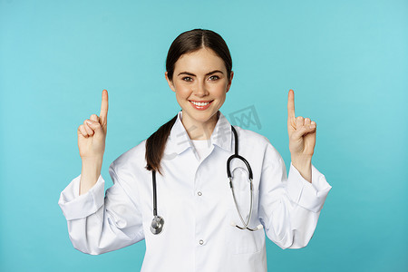自信的年轻女医生、穿大衣的医务人员的肖像，指指点点，微笑，展示药品广告、诊所促销、托瓦石背景